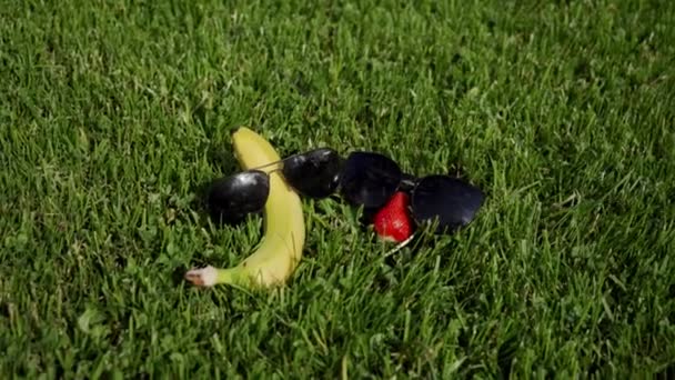 Fresa, plátano en gafas de sol descansan sobre hierba verde como pareja enamorada — Vídeo de stock