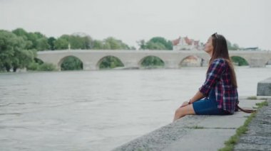 Ekose gömlekli gezgin kız setin üzerinde oturmuş, bacakları sarkık, Stone Bridge 'de.