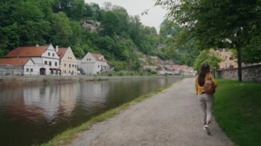 Sarı ceketli kız Krumlov 'da Vltava nehrinin setinde tek başına yürüyor.