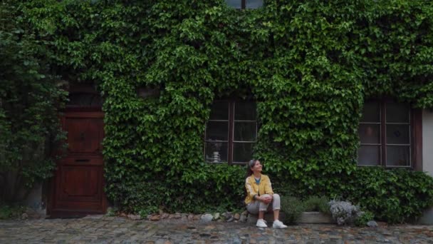 Meisje zit op een steen in de buurt van huis bedekt groeiende planten in fantastische stad Krumlov — Stockvideo