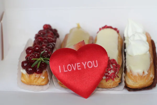 Traditionell fransk efterrätt med plysch hjärta och en inskription jag älskar dig. Vackra eclairs med isbildning och bär. — Stockfoto