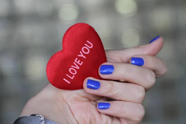 Vacker kvinnlig hand med manikyr håller ett plysch hjärta. Ljust blått nagellack. — Stockfoto