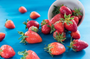 Mavi arka plan üzerinde ahşap masa üzerinde hasır sepet içinde olgun çilek