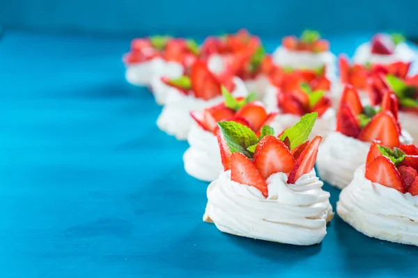 A small meringue Pavlova dessert with some strawberry slices with mint leaves on a blue background — Stock Photo, Image