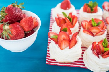 Küçük beze Pavlova tatlı nane ile bazı çilek dilimleri ile mavi bir arka plan üzerinde bırakır