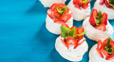 Küçük beze Pavlova tatlı nane ile bazı çilek dilimleri ile mavi bir arka plan üzerinde bırakır