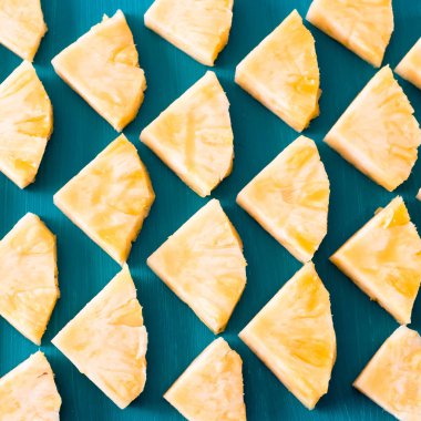 Bahar ya da yaz konsepti: bilmece birçok mavi ahşap masa arka plan üzerinde döşeme sarı ananas parçaları kadar yakın.