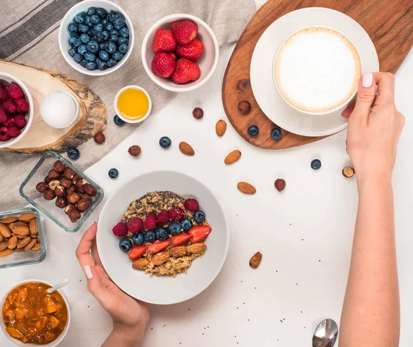 Günaydın - yulaf ezmesi kahve, çilek, yumurta, fındık ile sağlıklı kahvaltı arka plan. Kahve, eller, tutun, cup. Beyaz ahşap gıda arka plan, üstten görünüm