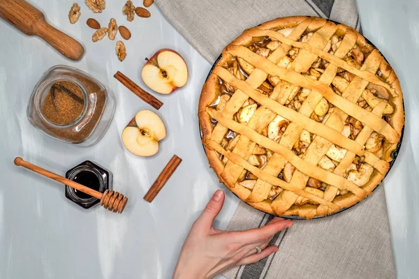 Apple pie on a gray kitchen towel. Hands put on the table. Apples, cinnamon, sugar, honey and nuts, top view — Stock Photo, Image