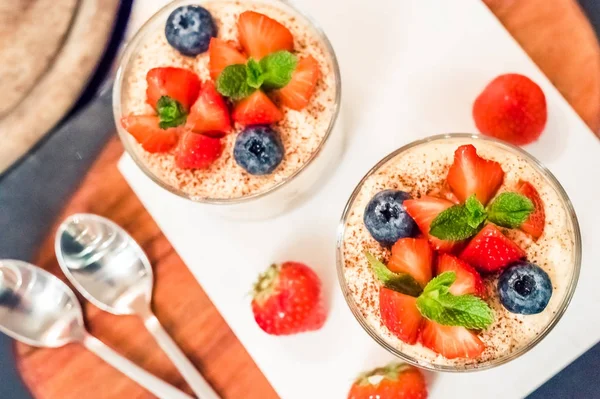 Homemade italian dessert tiramisu with strawberrie, blueberry, mint in glass jars, top view on a white background — Stock Photo, Image