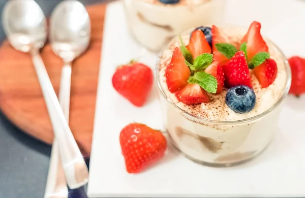 Tiramisu de sobremesa italiano caseiro com morango, mirtilo, hortelã em jarros de vidro, vista superior sobre um fundo branco — Fotografia de Stock