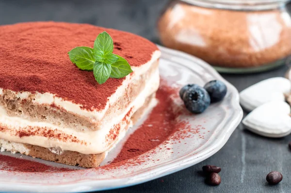 Italienisches Tiramisu-Dessert auf einem Porzellanteller auf schwarzem Hintergrund — Stockfoto