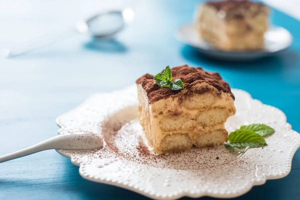 Italienisches Tiramisu-Dessert auf einem Porzellanteller, auf blauem Hintergrund — Stockfoto