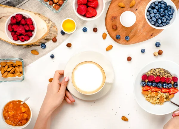 Доброе утро - здоровый завтрак с овсянкой кофе, ягодами, яйцом, орехами. Кофе, руки, держать, чашку. Белый деревянный пищевой фон, вид сверху — стоковое фото