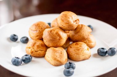 Ev yapımı profiterol ile yaban mersini beyaz tabakta servis