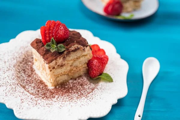 Stuk van tiramisu taart met munt en aardbeien op een blauwe achtergrond — Stockfoto