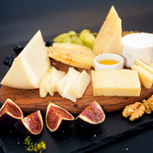Un plato de queso. Surtido de queso con nueces, almendras, uvas, higos, fresas, arándanos y miel en un plato de piedra — Foto de Stock
