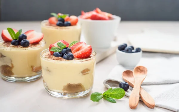 Homemade, exquisite dessert tiramisu in glasses decorated with strawberry, blueberry, mint on white wooden table — Stock Photo, Image