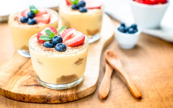 Homemade, exquisite dessert tiramisu in glasses decorated with strawberry, blueberry, mint on white wooden table — Stock Photo, Image