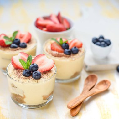 Gözlüklü ev yapımı, enfes tatlı tiramisu çilek, yaban mersini, nane ile dekore edilmiş beyaz tahta masada görünümü top.