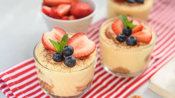 Caseiro, requintado tiramisu sobremesa em óculos decorados com morango, mirtilo, hortelã na mesa de madeira branca, vista superior . — Fotografia de Stock