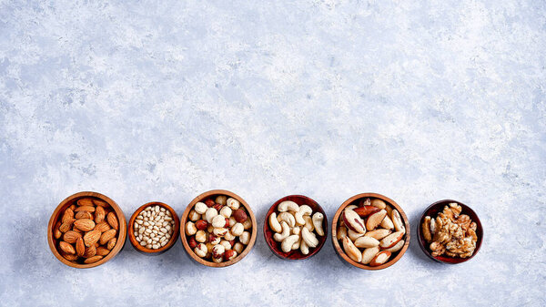 pecans, hazelnuts, almonds, pine nuts, Brazil nut, cashews in wooden bowls on blue background, top view, flat lay