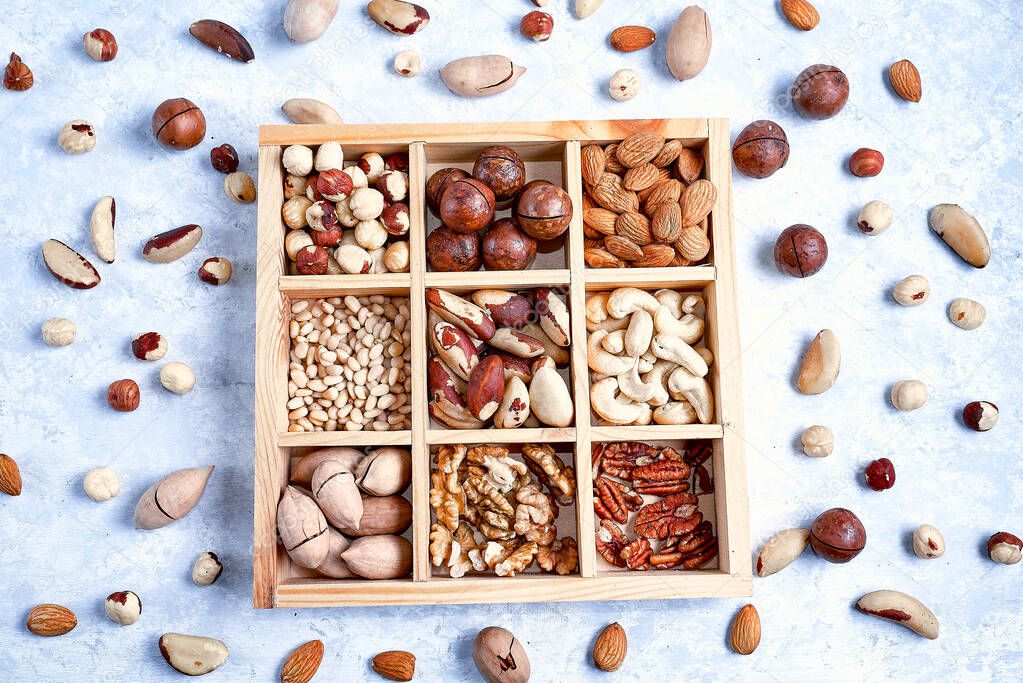 pecans, hazelnuts, almonds, pine nuts, brazil nut, cashews in a wooden box on blue background, top view, flat lay