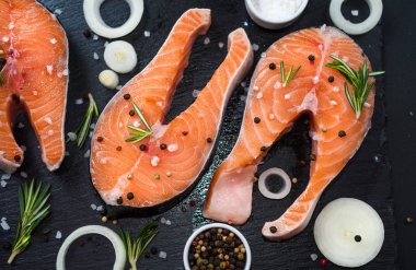 soğan, biberiye, baharat, konsept diyet, doymamış yağlar, omega 3 ile koyu taş arka plan üzerinde çiğ somon biftek