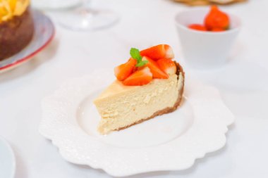 Beyaz festival masasında seramik tabakta taze çilekli cheesecake.
