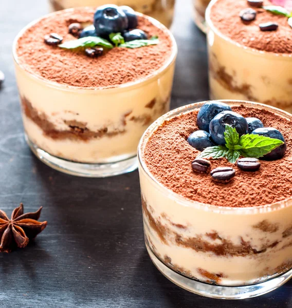 Изысканный десерт из тирамису в стакане, посыпанном какао и украшенном кофейными зернами на темном фоне, роскошный десерт — стоковое фото