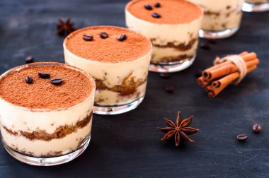 Koyu arkaplanda kahve çekirdekleri ve lüks bir tatlı serpiştirilmiş bir bardakta klasik tiramisu tatlısı.