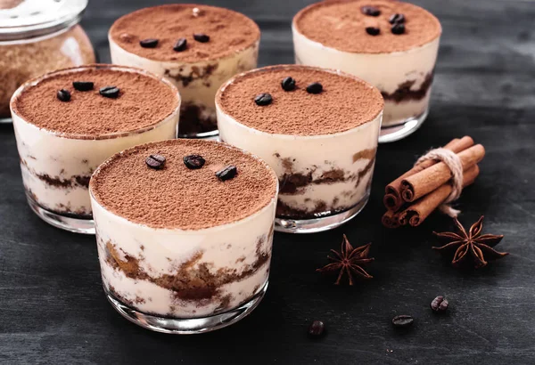 Sobremesa tiramisu clássico em um copo polvilhado com cacau e decorado com grãos de café em um fundo escuro, sobremesa de luxo — Fotografia de Stock