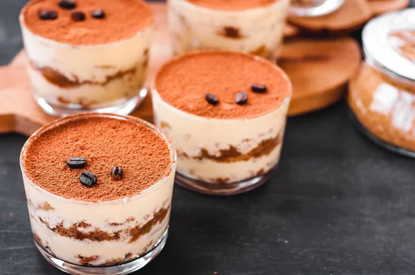 Classico dessert tiramisù in un bicchiere cosparso di cacao e decorato con chicchi di caffè su sfondo scuro, dessert di lusso — Foto Stock