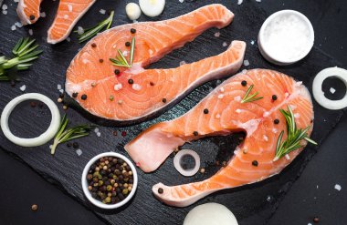 Çiğ balık bifteği, biber ve tuz, siyah taş beton masa üzerinde otlar, uzay manzarasını kopyala