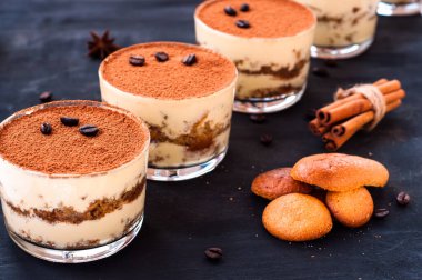 Koyu arkaplanda kahve çekirdekleri ve lüks bir tatlı serpiştirilmiş bir bardakta klasik tiramisu tatlısı.