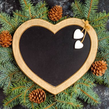 Yılbaşı ya da yeni yıl kompozisyonu, kalp şeklinde çerçeve ve noel dekorasyonu ve siyah tahta arka planda parıltılar, düz yatış. en üstteki görünüm