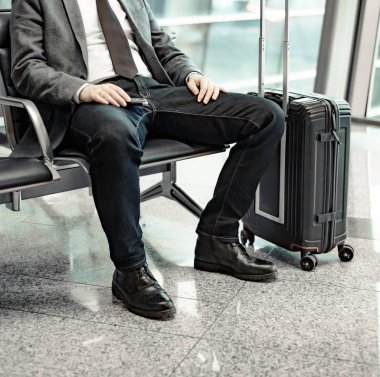 Adam havaalanında uçağını bekliyor ve cep telefonuna bakıyor.