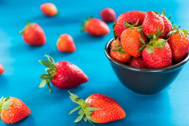 mavi bir arka planda bir kase üst görünümünde taze parlak çilek