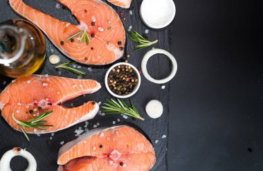 Çiğ balık bifteği, biber ve tuz, siyah taş beton masa üzerinde otlar, uzay manzarasını kopyala