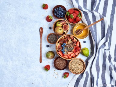 Sağlıklı kahvaltı ve kahvaltı malzemeleri, meyve ve çilek, incir, yaban mersini, çilek, keten ve chia tohumu, bal ile yulaf ezmesi. Üst görünüm, düz yatıyordu