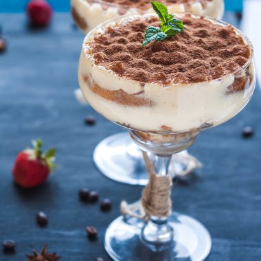 Koyu arkaplanda kakao tozuyla süslenmiş kokteyl bardaklarıyla süslü lüks tiramisu.