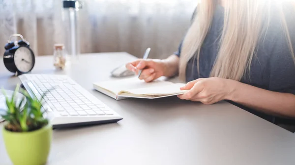 Une jeune fille s'assoit à un bureau et prend des notes dans un carnet — Photo