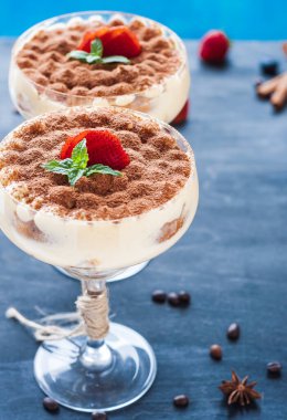 Ahşap arka planda kakaolu kokteyl bardağında lüks bir tiramisu tatlısı.