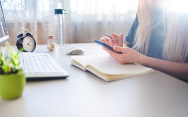 young woman sits at a desk and types on a smartphone