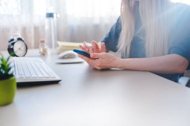 Genç bir kadın masada oturuyor ve akıllı telefondan yazı yazıyor.