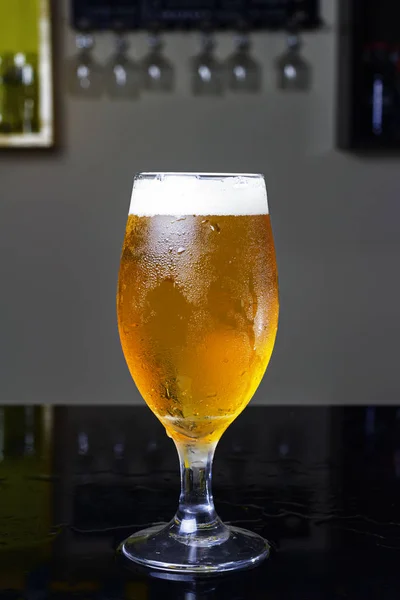 Bicchiere pieno di birra, con birra pilsen o chopp, su un tavolo nero in un pub — Foto Stock