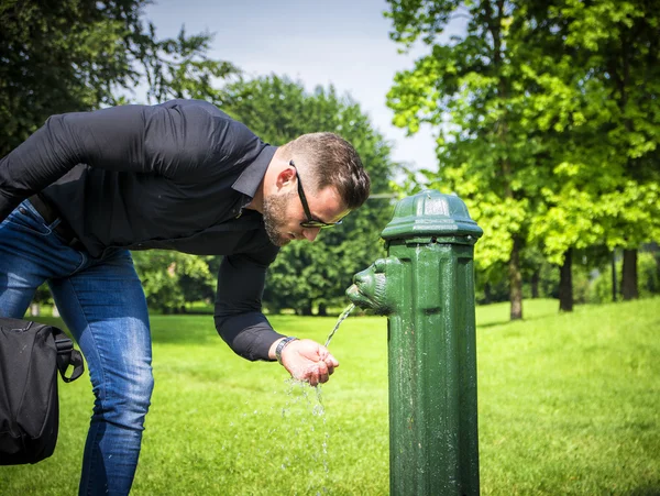 Vista laterale dell'uomo d'affari barbuto acqua potabile dalla Fontana del parco — Foto Stock