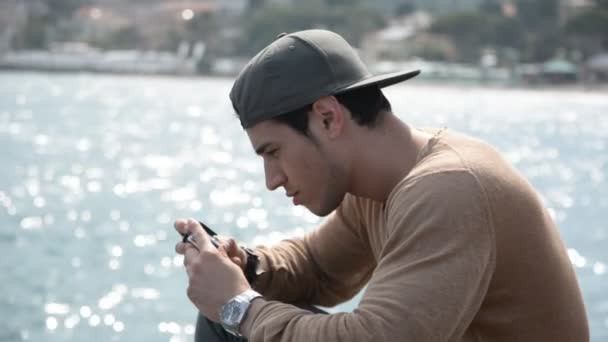 Атлетик на берегу моря использует мобильный телефон, чтобы напечатать сообщение — стоковое видео