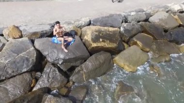 Deniz tarafından kayaya oturan genç gömleksiz atletik adam