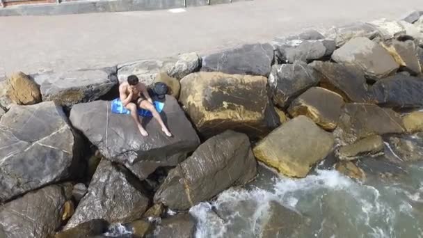 Молодий спортсмен без сорочки сидить на скелі біля моря — стокове відео
